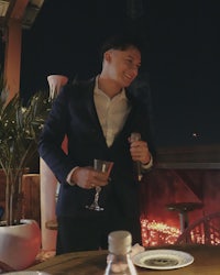 a man in a suit standing at a table holding a wine glass