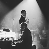 two men in tuxedos singing in front of a piano